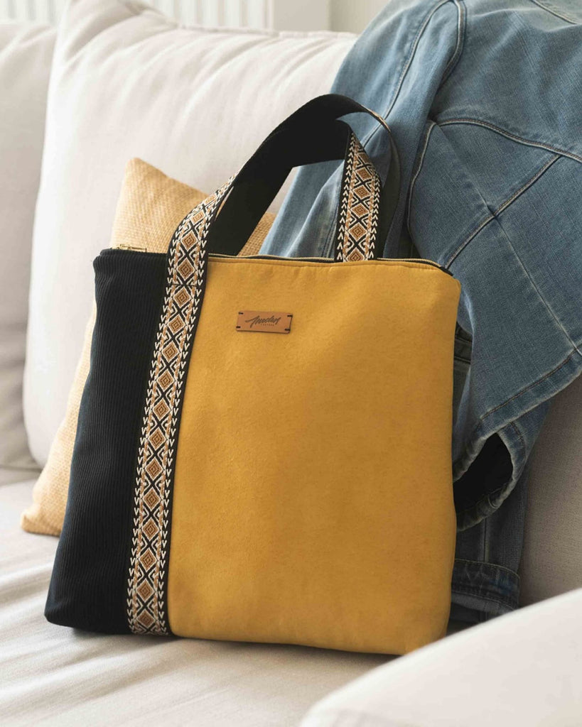 sac en tissu jaune et noir avec anses motifs ethniques, posé sur un canapé blanc.