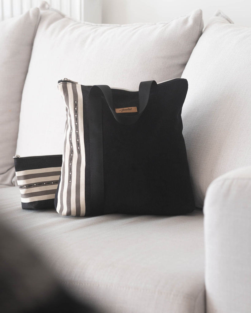 Sac à main velours noir et rayures avec trousse posés sur un canapé blanc