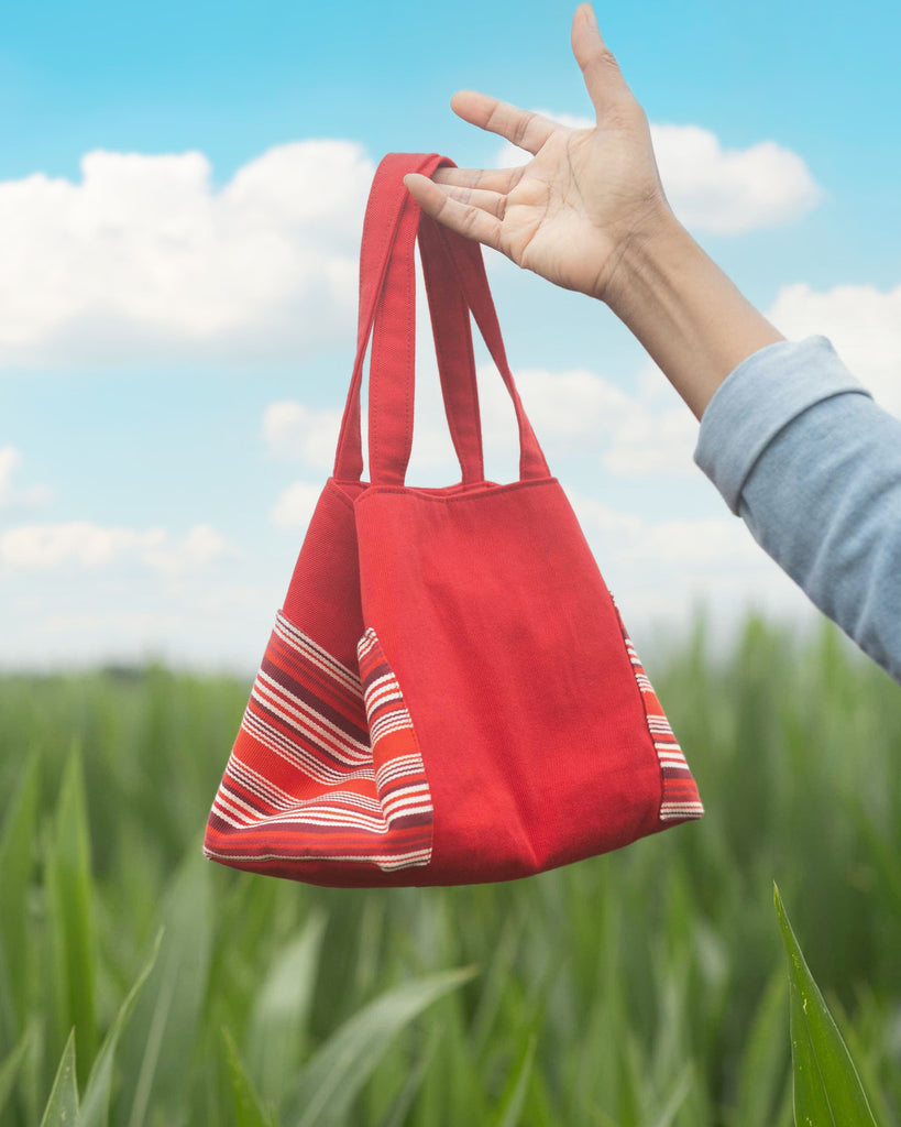 Sac rouge avec poches rayées tenuen l'ar au dessus d'un champ 