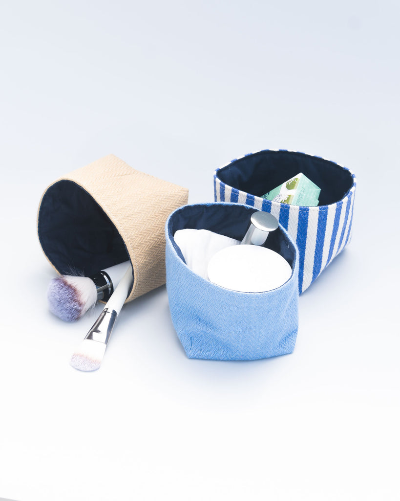 Trois petites panières tissu bleu, blanc, beige séparées contenant des effets de maquillage