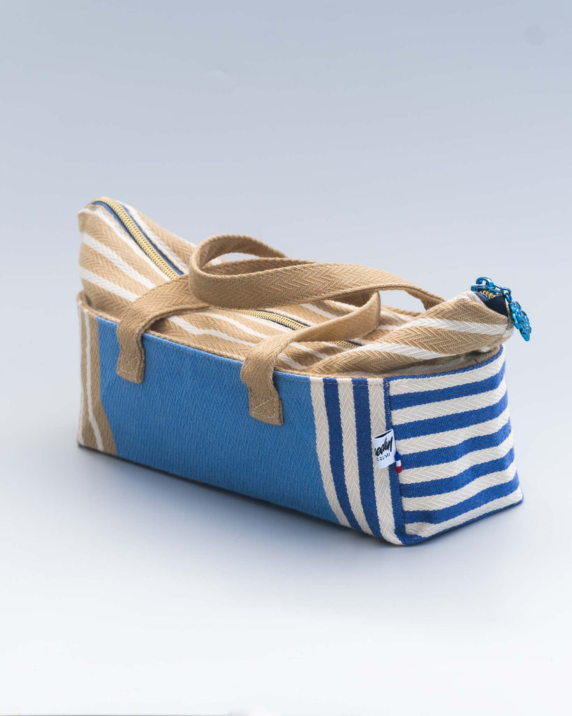 Trousse allongée en toile bleue et beige à rayures, fermée, posée sur un fond clair